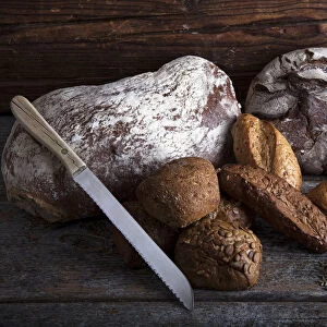 Bread loaves, rolls and a bread knife, rye grain and ears of corn on a rustic wooden surface