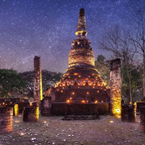 Old stupa with candlelight and milky way galaxy in the Kamphaeng Phet Historical Park