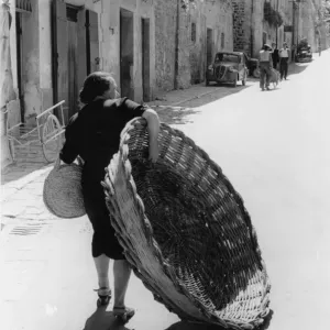 Giant Basket Print - Woman carrying a large wicker basket in Assisi Giant Basket Print - Woman carrying a large wicker basket in Assisi