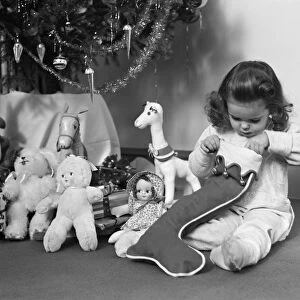 Young girl in pajamas, opening Christmas stocking next to Christmas tree. (Photo by H