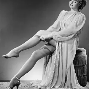 Young woman putting on stockings in studio (B&W)