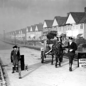 Milk man with his horse and float stands in a street where an unexploded bomb has