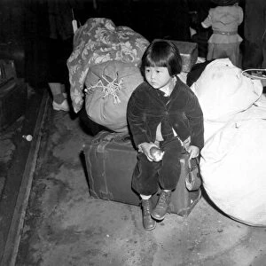 A young evacuee of Japanese ancestry waits for bus with family baggage