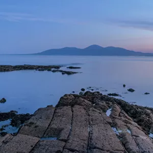Rocky shore on St Johns Point at sunset, mountains in distance across sea
