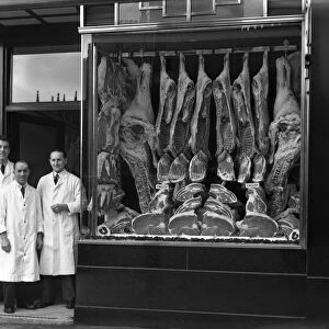 Butchers standing next to their shop window display, South Yorkshire, 1955. Artist