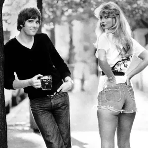 Actor Steve Alder holding a pint of beer as he poses with a model wearing denim hot pants