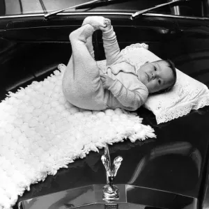 A baby girl lying on a mat on the bonnet of a Rolls poyce Silver Cloud car November