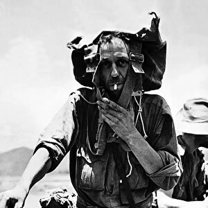 A British soldier uses his backpack to shade his head from the sun as he returns to India
