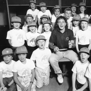 David Essex Singer surrounded by choir of school children wearing baseball caps