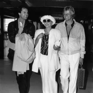 Joan Collins walking through Heathrow Airport with her boyfriend Peter Holm on her left