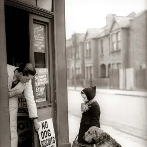 Little Girl wearing wooly hat, coat and scarf, standing outside corner shop grocers with