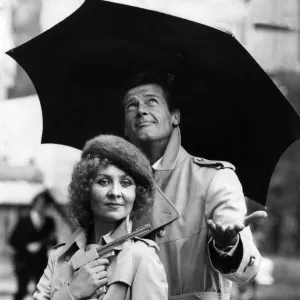 Lulu holding a Dunhill gun and Roger Moore together in the rain outside the Hilton Hotel