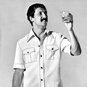 A man wearing a shirt with shorts looking at a glass of whisky