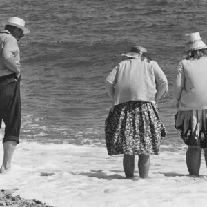 Dos mujeres ancianas y un hombre anciano con sombreros se encuentran en la playa con los pies en el agua. Dos mujeres ancianas y un hombre anciano con sombreros se encuentran en la playa con los pies en el agua.