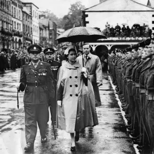 Queen Elizabeth II braves the rain with rain mac and umbrella to inspect a guard of