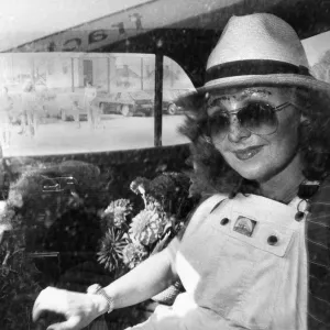 Singer Lulu in the back of a car wearing a trilby hat, sunglasses and dungarees