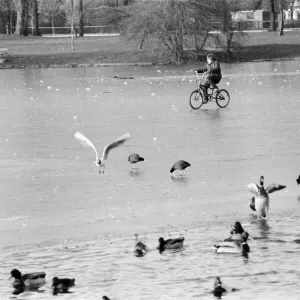 A young child riding his bike on the ice covered boating lake at Victoria Park in London