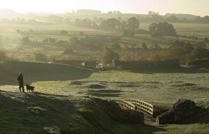<b class=qtipBold><figcaption>Castle Acre Castle N071221</figcaption></b><br>CASTLE ACRE CASTLE, Norfolk. Earthworks in the lower ward of the castle viewed from the north. A visitor pauses while walking his dog to look out over the early morning countryside.<br><em>© Historic England</em> Castle Acre Castle N071221