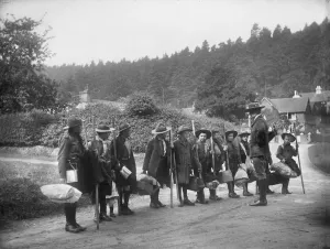 Prints of A line of boy scouts and their scout master standing on a road in Holmbury St Mary, Surrey. The scouts are carrying scout staffs and bedrolls for a camping or pioneering trip Historic Images 1920s To 1940s Prints: Print of Boy Scouts and Scout Master in Holmbury St Mary, Surrey
