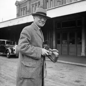 Prints of BOURNEMOUTH CENTRAL STATION, BOURNEMOUTH, DORSET. A portrait of John Laing holding a Rolleiflex camera outside Bournemouth train station, during a staff outing of Laings London office to Bournemouth Iconic Photographers of England - Historic Image Collections: Print of a man holding a camera outside Bournemouth Central Station