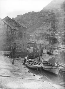 Prints of Staithes Beck, Loftus, Redcar and Cleveland. A man standing by a moored rowing boat. Photographed in the early 20th century by Edwin Dockree Then and Now England - Historic Change Over Time: Early 20th-century print of a man standing by a moored rowing boat
