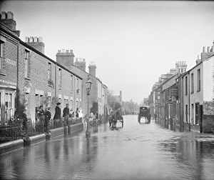 <b class=qtipBold><figcaption>Flooded street CC73_00433</figcaption></b><br>Lake Street, New Hinksey, Oxford, Oxfordshire. Looking down the street during a flood with people standing outside their houses and two carts making their way down the road. The Crown Inn is to the right. Photographed in 1890 by Henry W Taunt.<br><em>© Historic England Archive</em> Flooded street CC73_00433