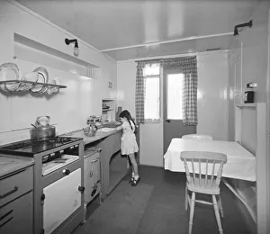 <b class=qtipBold><figcaption>Girl in prefab kitchen P_H00049_007</figcaption></b><br>A young girl in the kitchen of a Uni-Seco prefabricated house in Lyham Road, Brixton, London. 22nd September 1945. Ministry of Works. Prefabricated houses were constructed in Lyham Road and other similar sites in the area, in spaces left between older houses, where buildings had been destroyed by bombing.<br><em>© Historic England Archive</em> Girl in prefab kitchen P_H00049_007