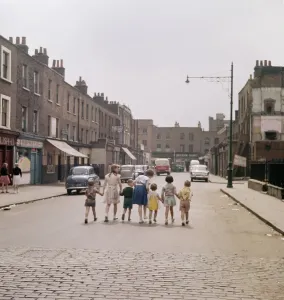 Prints of WHITE CONDUIT STREET, Islington, London. A line of children hold hands as they walk along the middle of White Conduit Street towards the junction with Chapel Market in Islington Then and Now England - Historic Change Over Time: Print of White Conduit Street, Islington