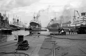 Prints of KING GEORGE V DOCK, Canning Town, London. Shipping in the dock with dock workers standing on the dockside in the foreground (mid 20th century) Related Prints: King George V Dock Print: A mid-20th-century photograph of a London dock