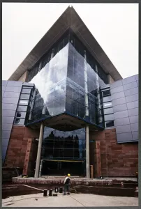 Prints of The Bridgewater Hall, Barbirolli Square, Manchester. Looking up at the glazed projecting prow of the main foyer of the Bridgewater Hall during its construction, with a workman in the foreground Engineering And Construction Prints: Print of The Bridgewater Hall's Main Foyer Under Construction