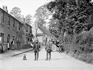 <b class=qtipBold><figcaption>Travelling performers CC71_00073</figcaption></b><br>TAPLOW, Buckinghamshire. Looking down a street in the village with two travelling punchinellos or performers, one with a monkey companion and the other a 'one man band'. Photographed by Henry Taunt in 1885.<br><em>© Historic England</em> Travelling performers CC71_00073