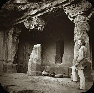 A bearded man stands in front of 3 ornately carved columns A bearded man stands in front of 3 ornately carved columns