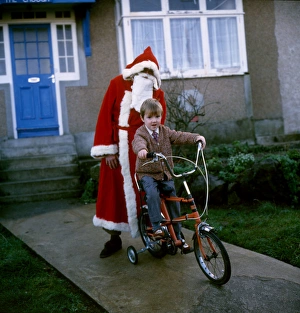 Father Christmas stands behind boy on bike Father Christmas stands behind boy on bike