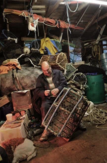 A fisherman mends a lobster pot in his waterside shed