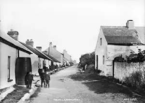 Prints of The Hill, Groomsport - a village street scene looking up with buildings either side and three small boys in the foreground, beside a barrel. (Location: Northern Ireland: County Down: Groomsport) Down Prints: Early 20th Century Print of Groomsport Village Street Scene