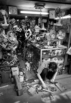 Man squats on floor of his streetside workshop, Hong Kong Man squats on floor of his streetside workshop, Hong Kong