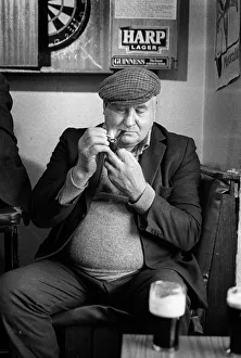 Mature man wearing cloth cap lights his pipe in an Irish pub Mature man wearing cloth cap lights his pipe in an Irish pub