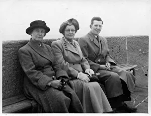 Two mature women with a younger man pose for a snap on a bench along the sea front at an Two mature women with a younger man pose for a snap on a bench along the sea front at an