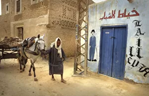 Muslim man leads mule and cart through the streets of Nefta