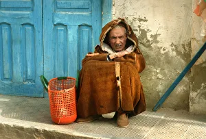 Old man wearing a djelleba sits on pavement, Tunisia Old man wearing a djelleba sits on pavement, Tunisia