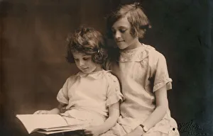 Aids Gallery: Older girl helps her younger sister read a book