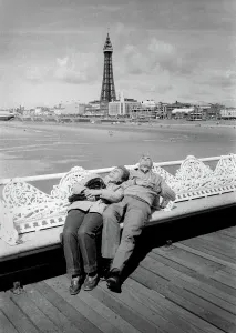 Prints of An elderly couple lie back on the wrought iron seats on Blackpool Pier for a snooze. The beach and Blackpool Tower are in the background. Date: circa 1970 Lancashire Prints: Blackpool Pier Scene Print circa 1970