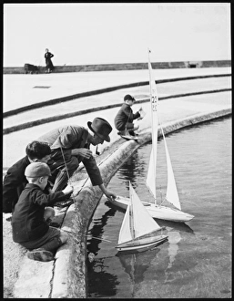 <b class=qtipBold><figcaption>Playing with Model Boats</figcaption></b><br>MODEL BOATS A father and his boys launch their model yachts upon the West Shore Pool at Llandudno, Wales<br><em>© Mary Evans Picture Library/GERALD WILSON</em> Playing with Model Boats