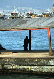 Silhouette of man sat on a bollard on a pier in Hong Kong Silhouette of man sat on a bollard on a pier in Hong Kong