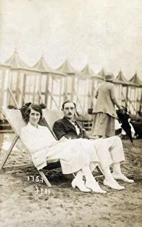 Smart young couple sat on the beach in deckchairs Smart young couple sat on the beach in deckchairs