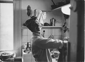A smiling young woman in a headscarf and apron washing up or preparing food in a kitchen A smiling young woman in a headscarf and apron washing up or preparing food in a kitchen