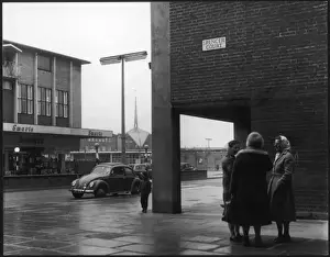 Prints of A typical English street in Corby, Northamptonshire, on a rainy shopping day: three women stand chatting Northamptonshire Prints: Social Street Scene Print: Rainy Day in 1960s Corby