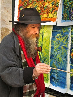 A street artist, with a long beard smoking a large pipe