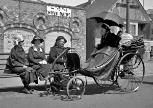 <b class=qtipBold><figcaption>Street scene near Hove Baths, Sussex</figcaption></b><br>Street scene near the Hove Baths in Sussex. Three women sit on a bench, near an elderly woman in an elaborate four-wheeled bath chair, shaded from the sun by a black umbrella. Date: 1920s<br><em>© Mary Evans Picture Library/John Maclellan</em> Street scene near Hove Baths, Sussex