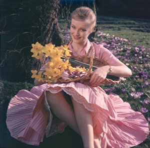 <b class=qtipBold><figcaption>Woman with Daffodils</figcaption></b><br>Pretty blonde woman in a pink shirtwaister dress with full, finely pleated skirt, holds a basket full of daffodils as she sits on the grass surrounded by crocii.<br><em>© Mary Evans Picture Library</em> Woman with Daffodils